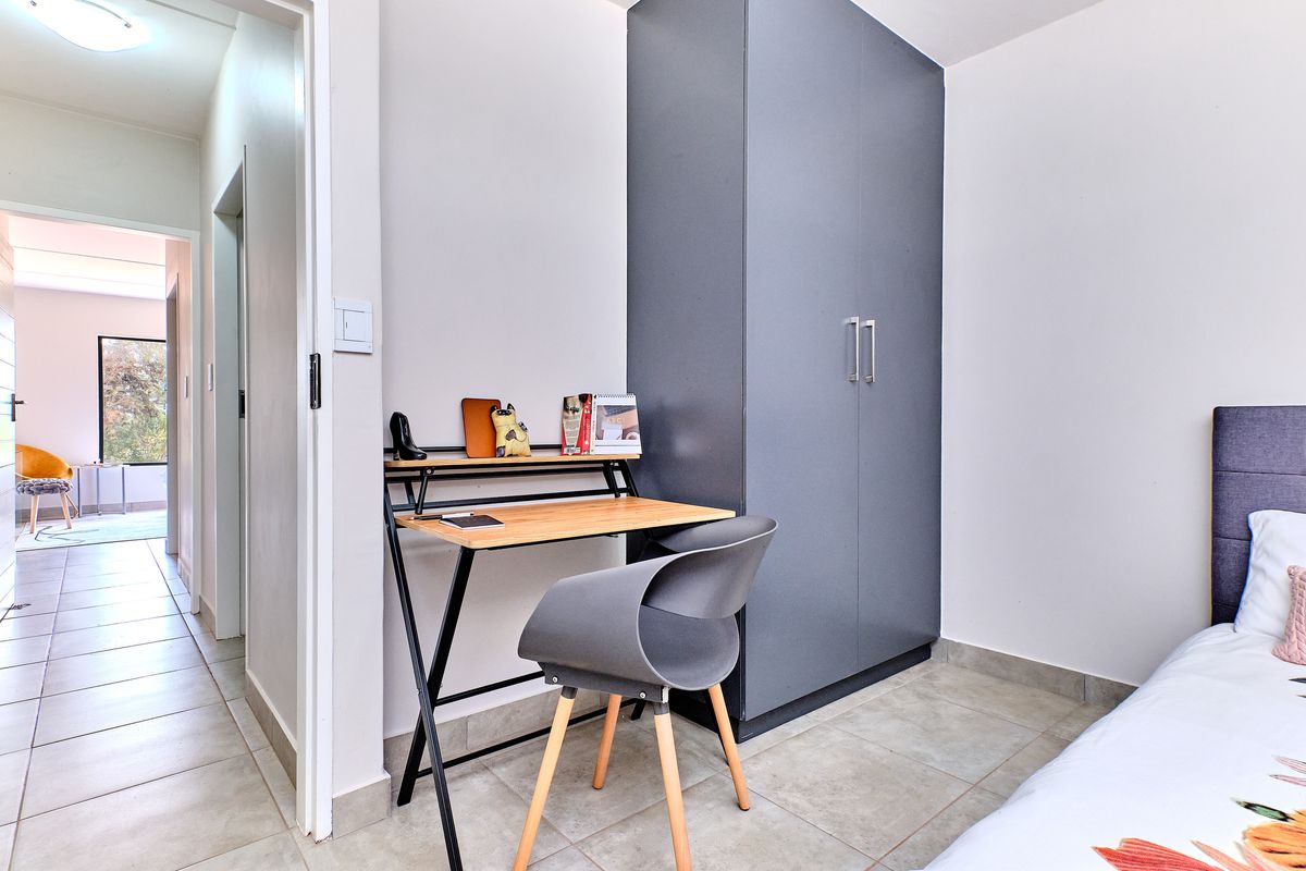 A bedroom featuring a built-in grey wardrobe and tiled flooring, with an adjacent hallway view.
