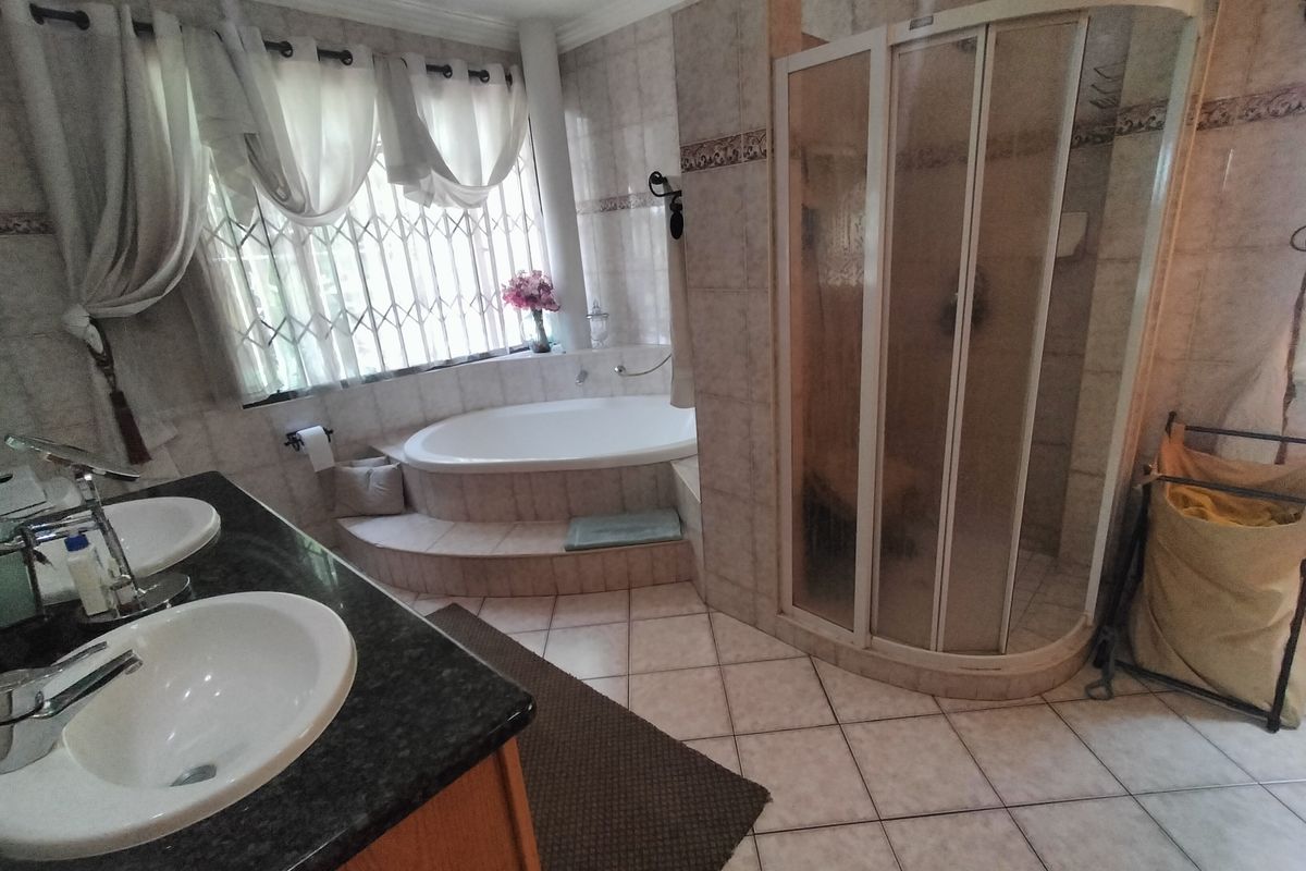 A spacious bathroom featuring a double vanity, a built-in corner bathtub, and a separate shower enclosure with tiled finishes throughout.