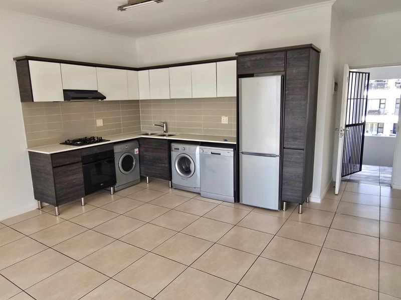 Modern kitchen featuring two-tone cabinetry, gas hob, under-counter oven, and tiled flooring, with an adjacent security gate leading to the exterior.