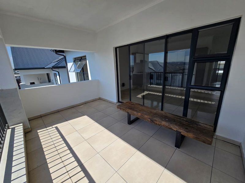 A spacious covered balcony featuring neutral floor tiles, a metal balustrade, and large sliding glass doors providing access to the interior living area.