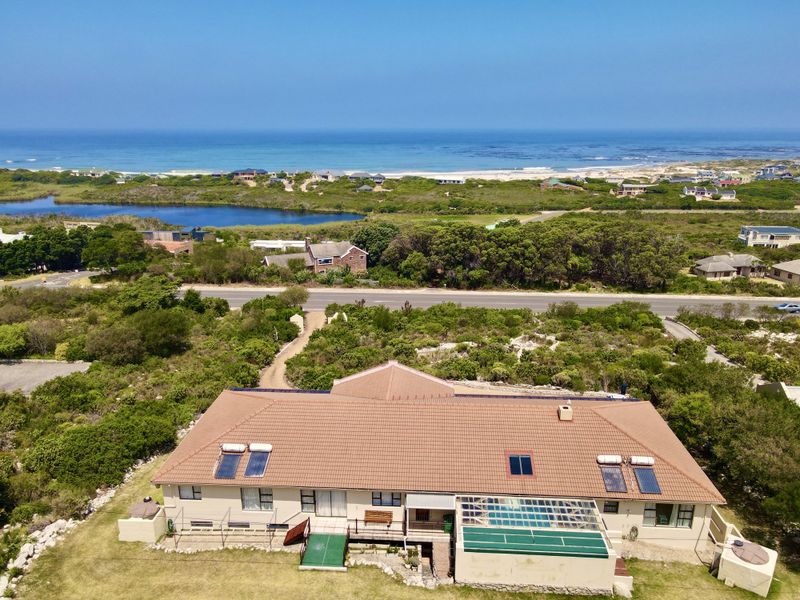 Aerial view of a coastal property featuring a tiled roof with solar panels, a swimming pool, and expansive views of the surrounding landscape and ocean.