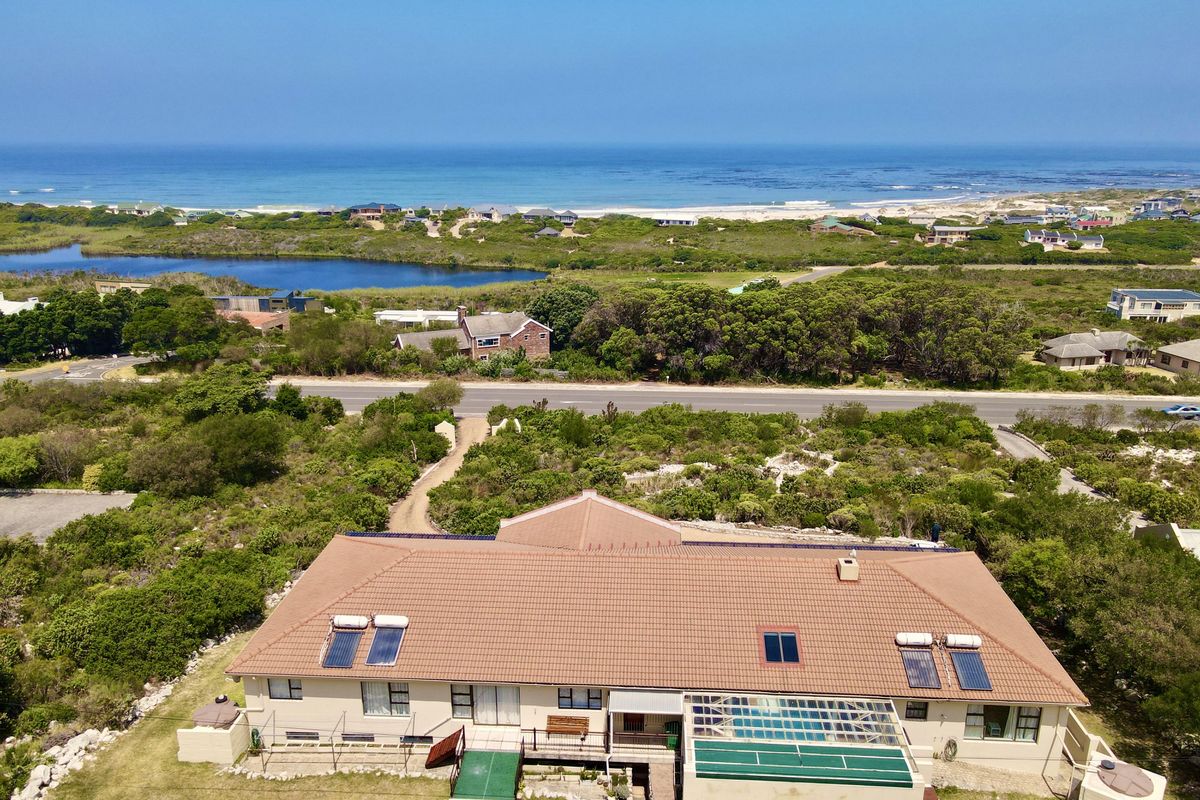 Aerial view of a coastal property featuring a tiled roof with solar panels, a swimming pool, and expansive views of the surrounding landscape and ocean.