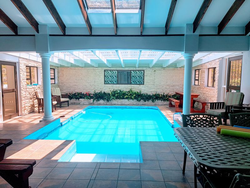 A spacious indoor swimming pool area featuring stone-clad walls, exposed timber beams, a large skylight, and tiled flooring, perfect for year-round entertainment.