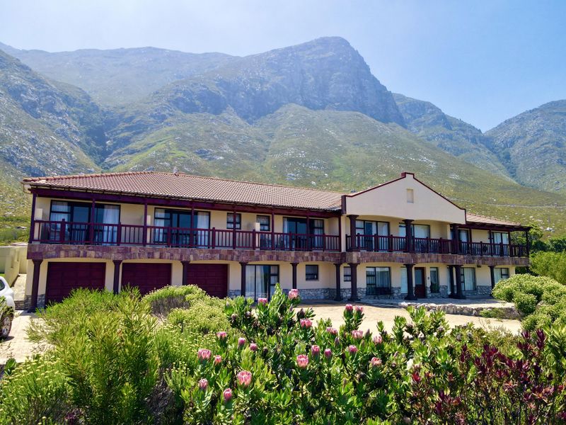 Spacious two-story residence featuring a terracotta tile roof, stone cladding, and a large balcony, set against a dramatic mountain backdrop.