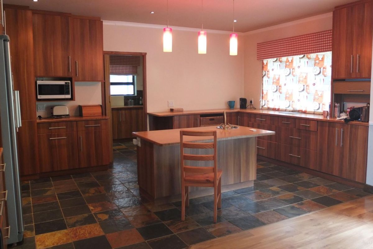 Spacious kitchen featuring wood-finish cabinetry, a central island with a sink, stone tile flooring, and integrated microwave, offering a functional layout with ample storage.