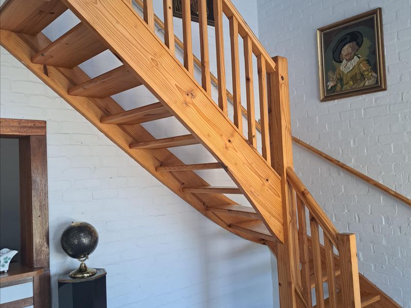 A bright hallway featuring a prominent timber staircase with matching balustrade, set against a white painted brick wall and tiled flooring.