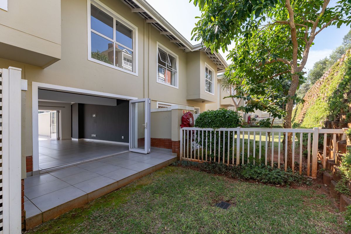 Rear view of the townhouse featuring a tiled patio area, bi-fold doors leading to the interior, and a private garden with a retaining wall.