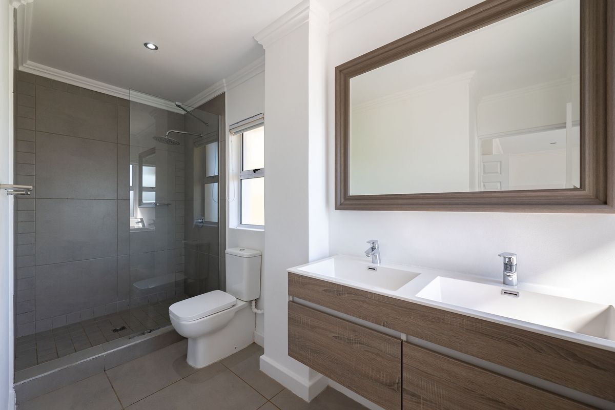 Modern bathroom featuring a double vanity with wood-look cabinetry, a large framed mirror, and a spacious walk-in shower with grey tiling.