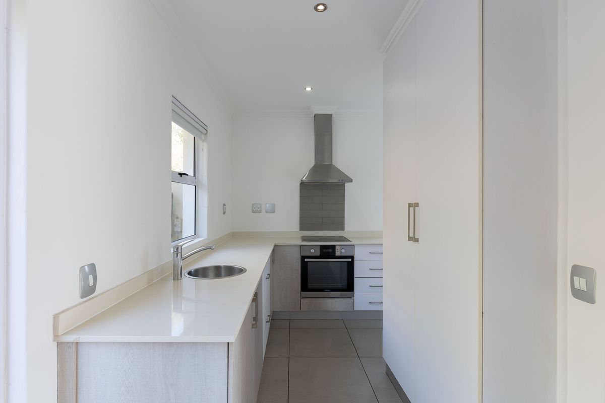 A modern, clean-lined kitchen featuring light-toned cabinetry, stone countertops, a stainless steel oven, hob, and extractor fan, with neutral floor tiling.