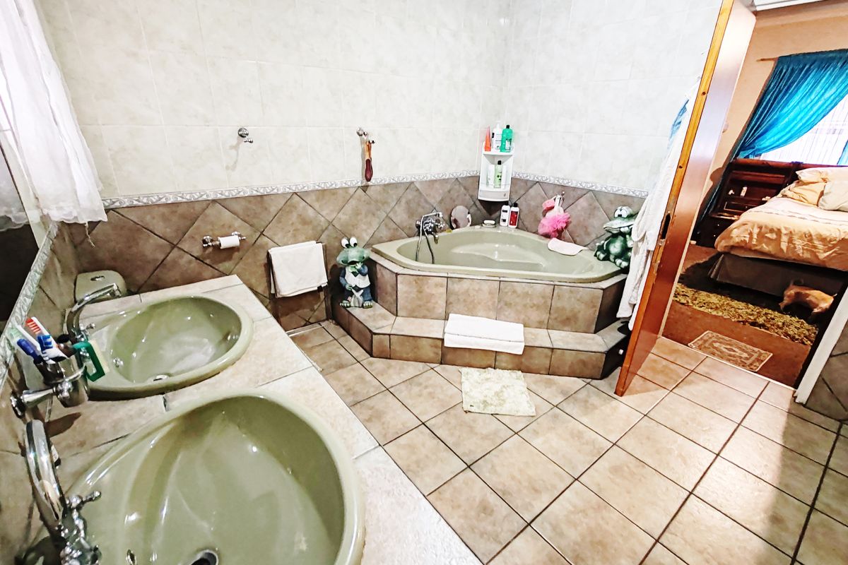 A spacious bathroom featuring a double vanity with integrated sinks and a raised corner bathtub, finished with neutral ceramic tiling throughout.