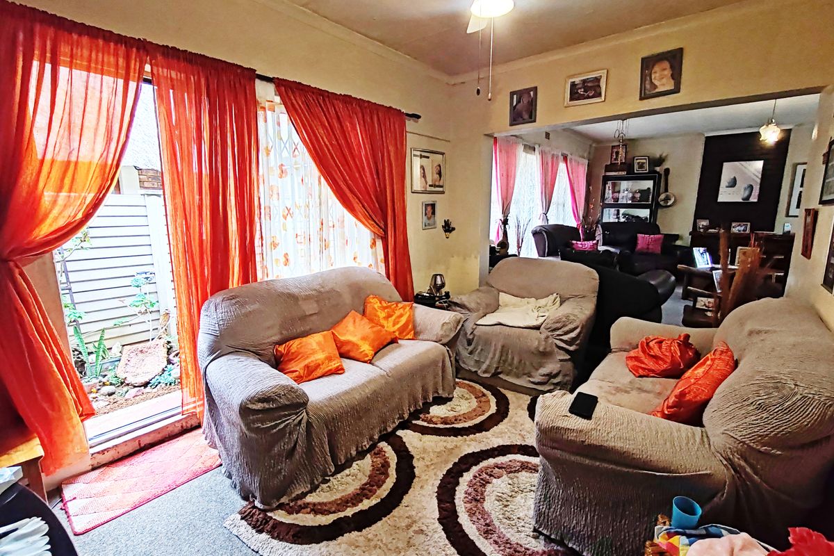 A living room area featuring a ceiling fan and sliding glass door access to the exterior, showing signs of wear on the ceiling and walls.