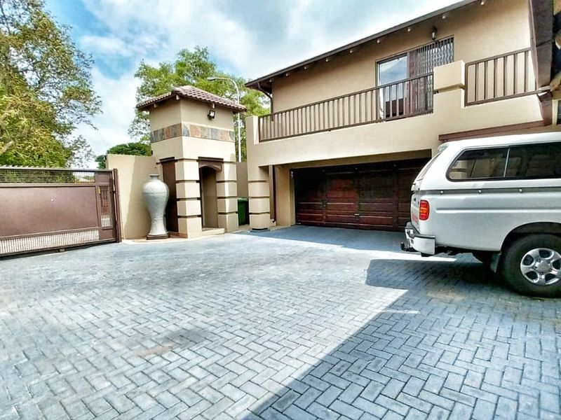 Front exterior view featuring a paved driveway, secure sliding gate, double garage, and an upper-level balcony with metal railings.