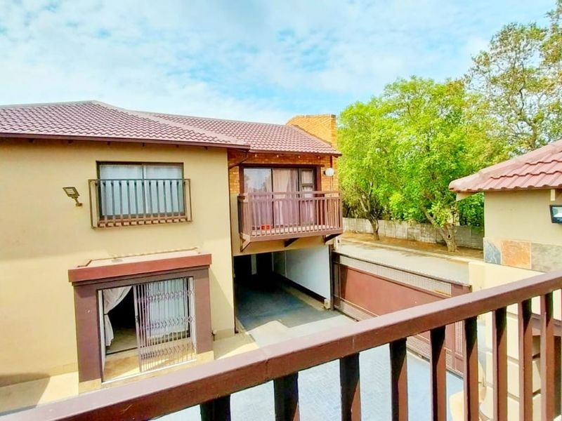 Rear view of a two-story residential property featuring a balcony, tiled roof, and paved driveway area.