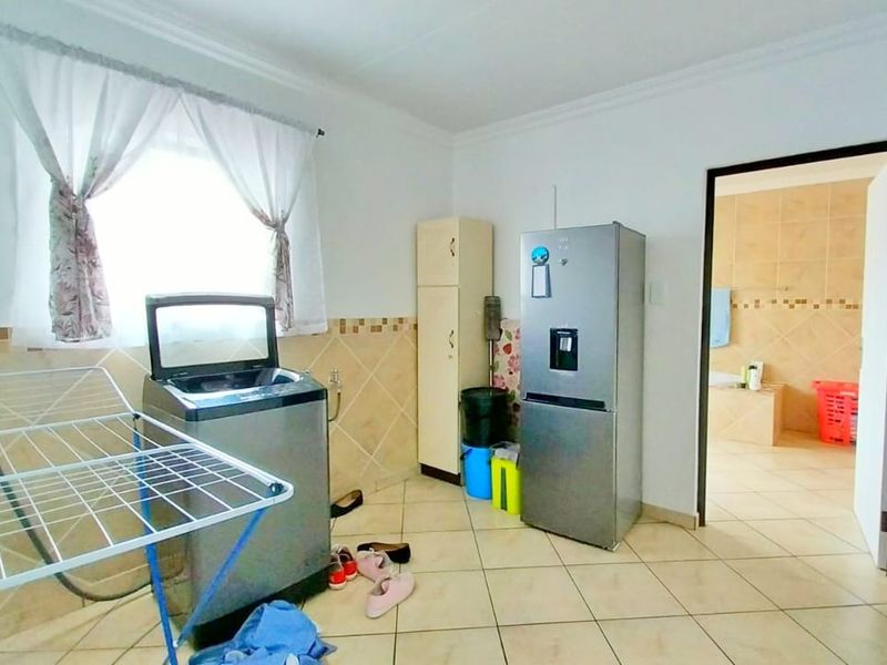 A functional laundry room featuring tiled flooring, tiled splashbacks, and dedicated plumbing connections for appliances, with direct access to an adjacent bathroom.