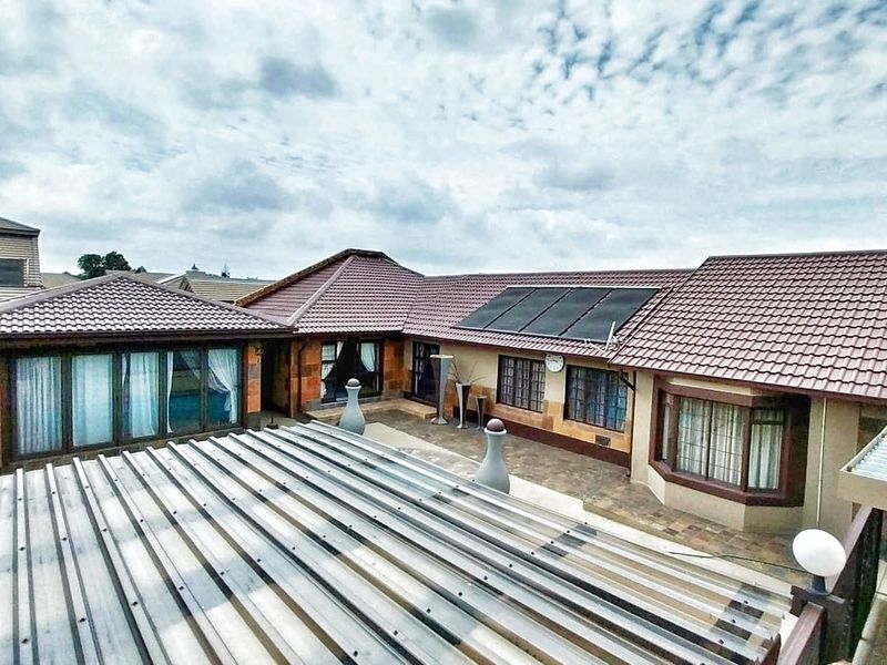 Rear view of the house featuring a paved courtyard, tiled roofing, and integrated solar panels.