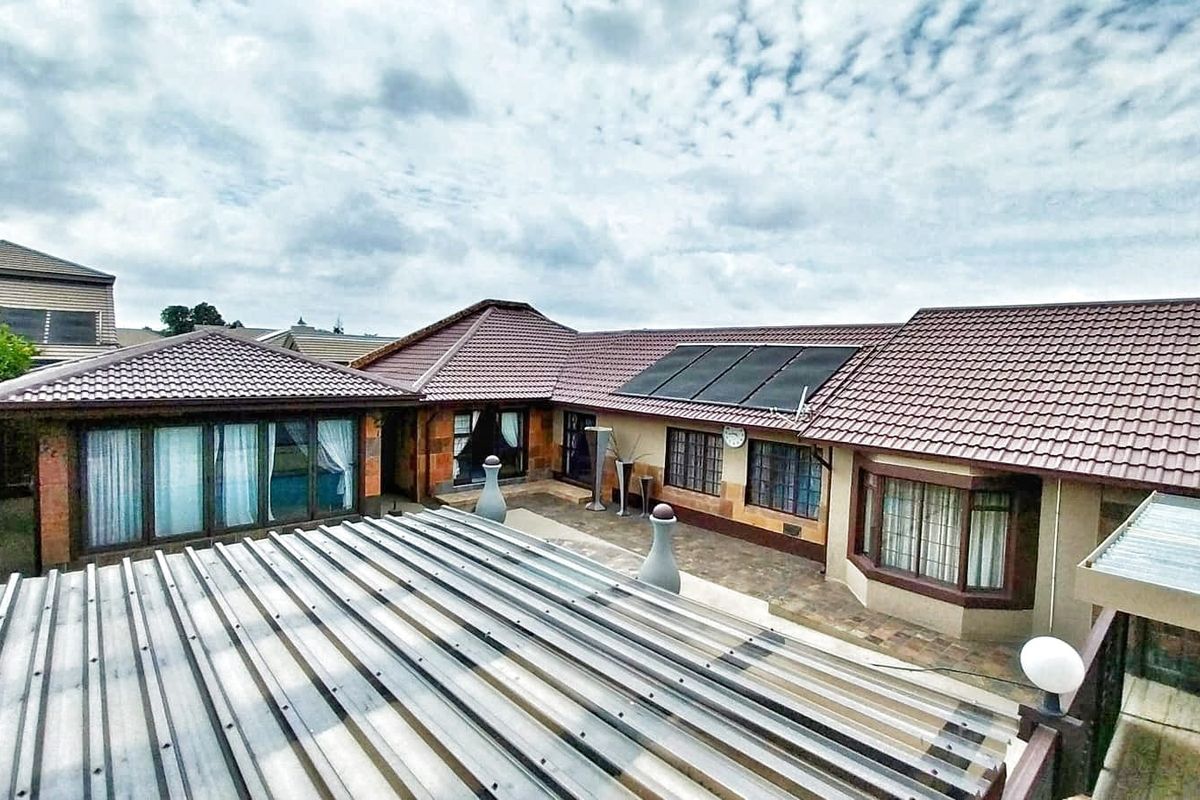 Rear view of the house featuring a paved courtyard, tiled roofing, and integrated solar panels.