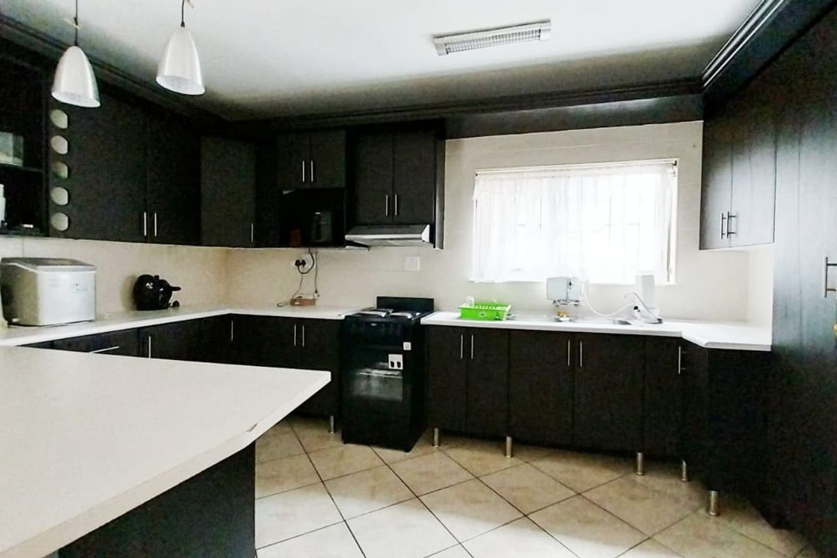 A functional kitchen featuring dark wood cabinetry, white countertops, a freestanding oven with extractor fan, and tiled flooring.