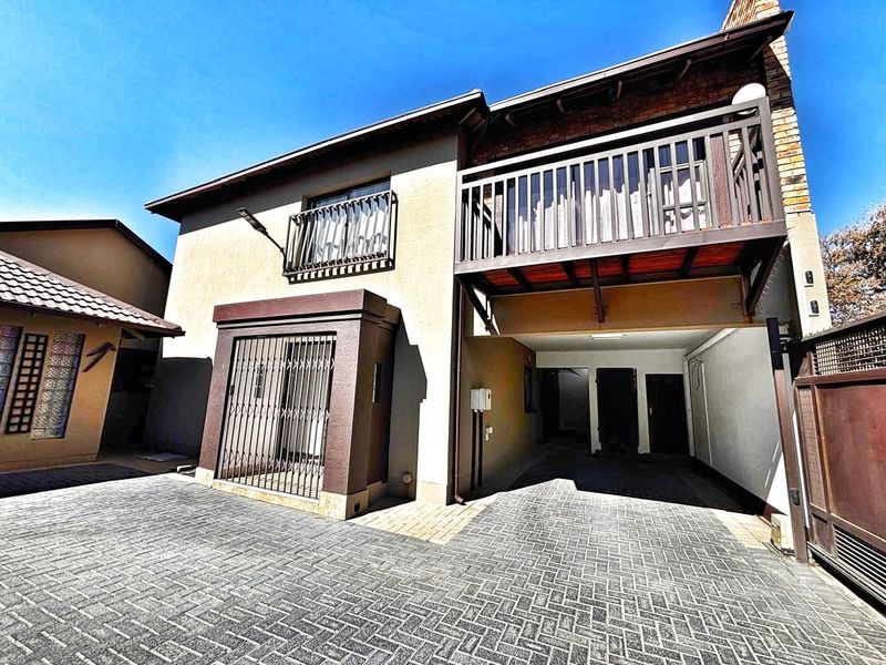 Front exterior view of the property featuring a paved driveway, secure gated entrance, and an upper-level balcony with wooden railings.
