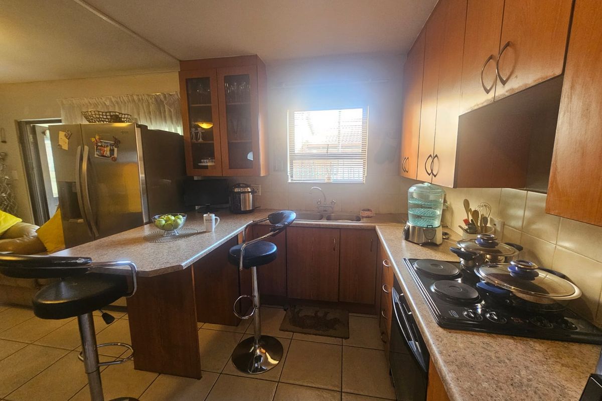 A functional kitchen featuring wood-tone cabinetry, laminate countertops, a breakfast bar, and integrated electric cooking appliances with ceramic tiled flooring.
