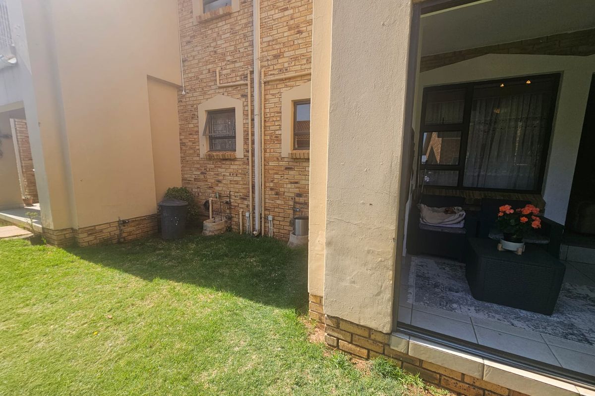 Rear view of the apartment featuring a face brick facade, a small private lawn, and a covered patio area with sliding door access.