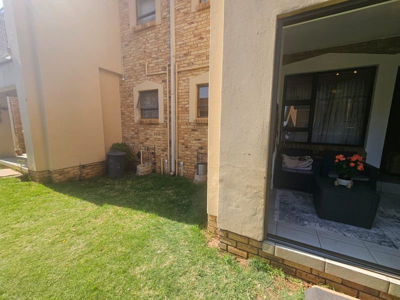 Rear view of the apartment featuring a face brick facade, a small private lawn, and a covered patio area with sliding door access.