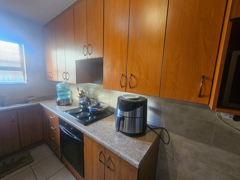 A functional kitchen featuring wood-look laminate cabinetry, stone-patterned countertops, a built-in oven with electric hob, and neutral ceramic tile backsplash and flooring.