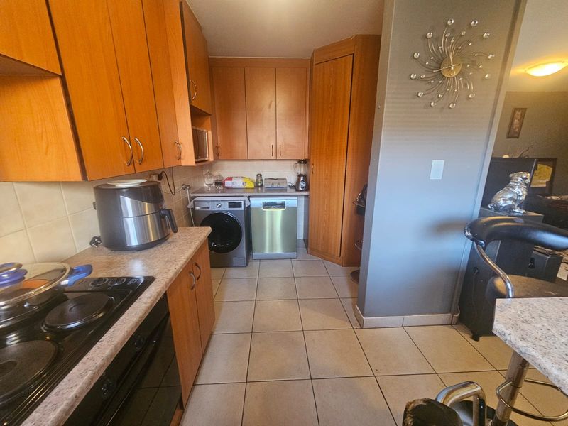 Functional kitchen featuring wood-look cabinetry, tiled flooring, built-in oven, and electric hob with integrated space for laundry appliances.