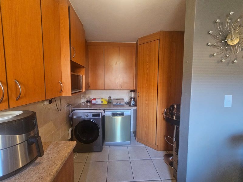 A functional kitchen featuring wood-look laminate cabinetry, tiled flooring, and a tiled backsplash with space for under-counter appliances.