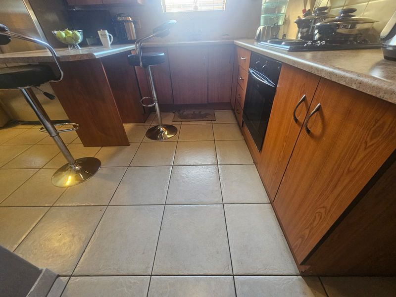 A functional kitchen featuring wood-look cabinetry, tiled flooring, built-in oven, and hob with ample counter space.
