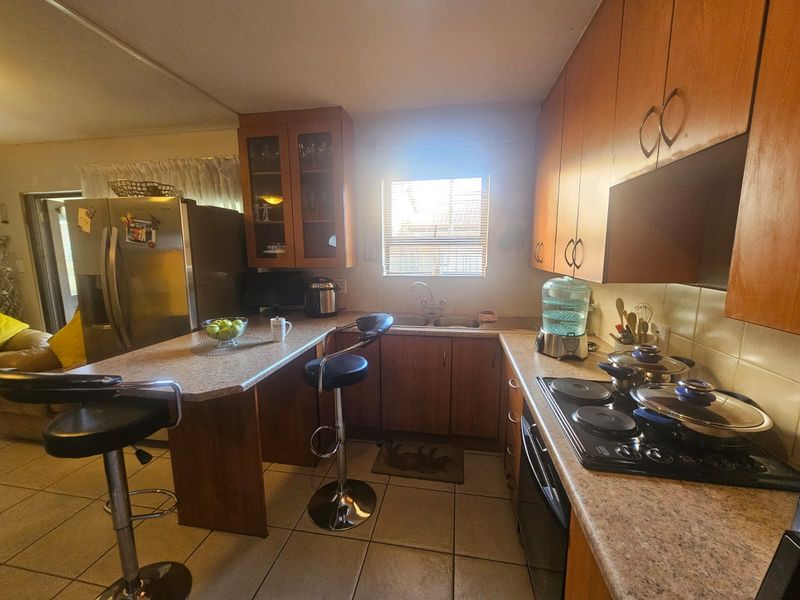 A functional kitchen featuring wood-tone cabinetry, laminate countertops, a breakfast bar, and integrated electric cooking appliances with ceramic tiled flooring.