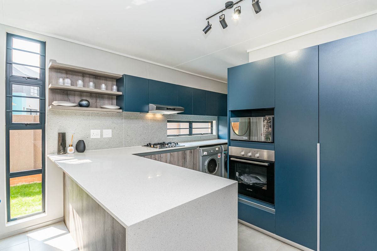 Modern kitchen featuring sleek blue cabinetry, quartz countertops, built-in oven and microwave, gas hob, and integrated laundry space with tiled flooring.