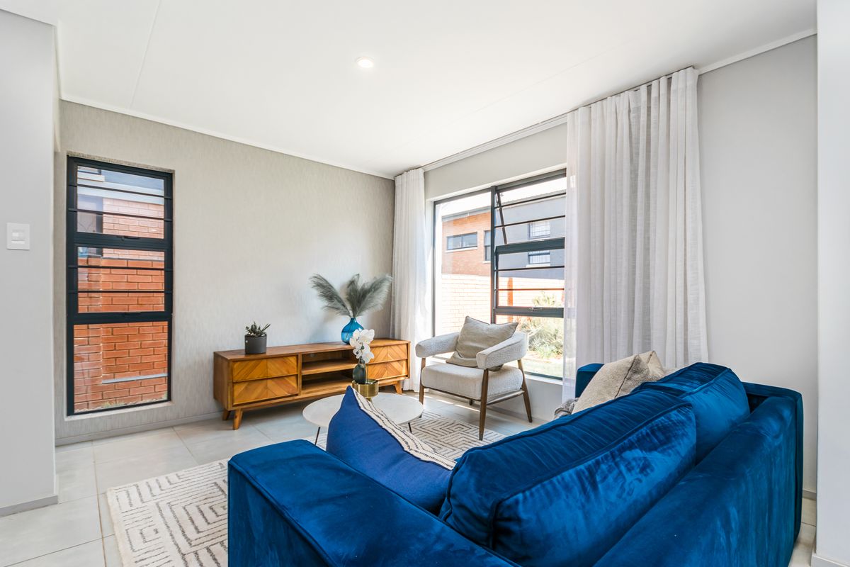 A bright and modern living room featuring neutral tiled flooring, large aluminium-framed windows, and recessed downlighting, creating a clean and inviting atmosphere.