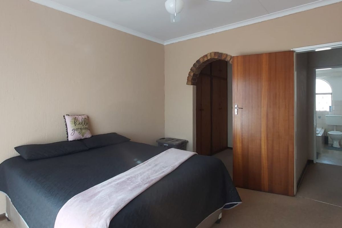 Spacious bedroom featuring built-in cupboards, a unique brick archway, and an adjoining en-suite bathroom, offering a functional layout with potential for modern updates.