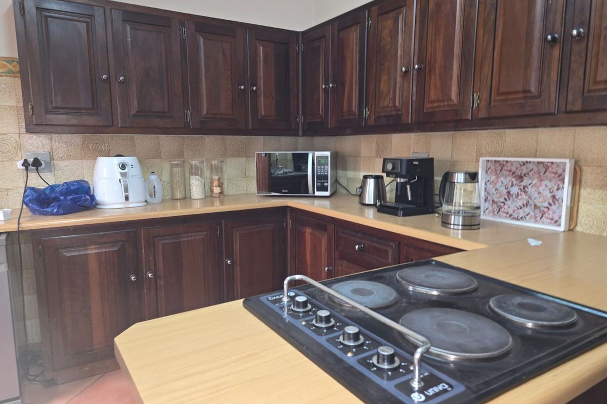 A functional kitchen featuring dark wood cabinetry, laminate countertops, and a built-in electric hob with a tiled backsplash.