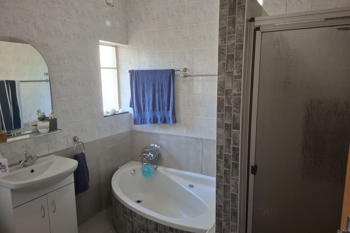 A functional bathroom featuring a built-in corner bathtub, a separate shower enclosure, and a vanity basin with wall-mounted mirror.