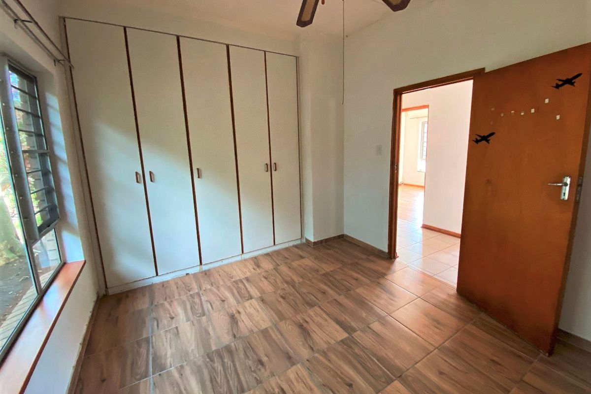 A bright, empty bedroom featuring wood-look tiled flooring, built-in cupboards, and a ceiling fan, offering a clean and functional space.