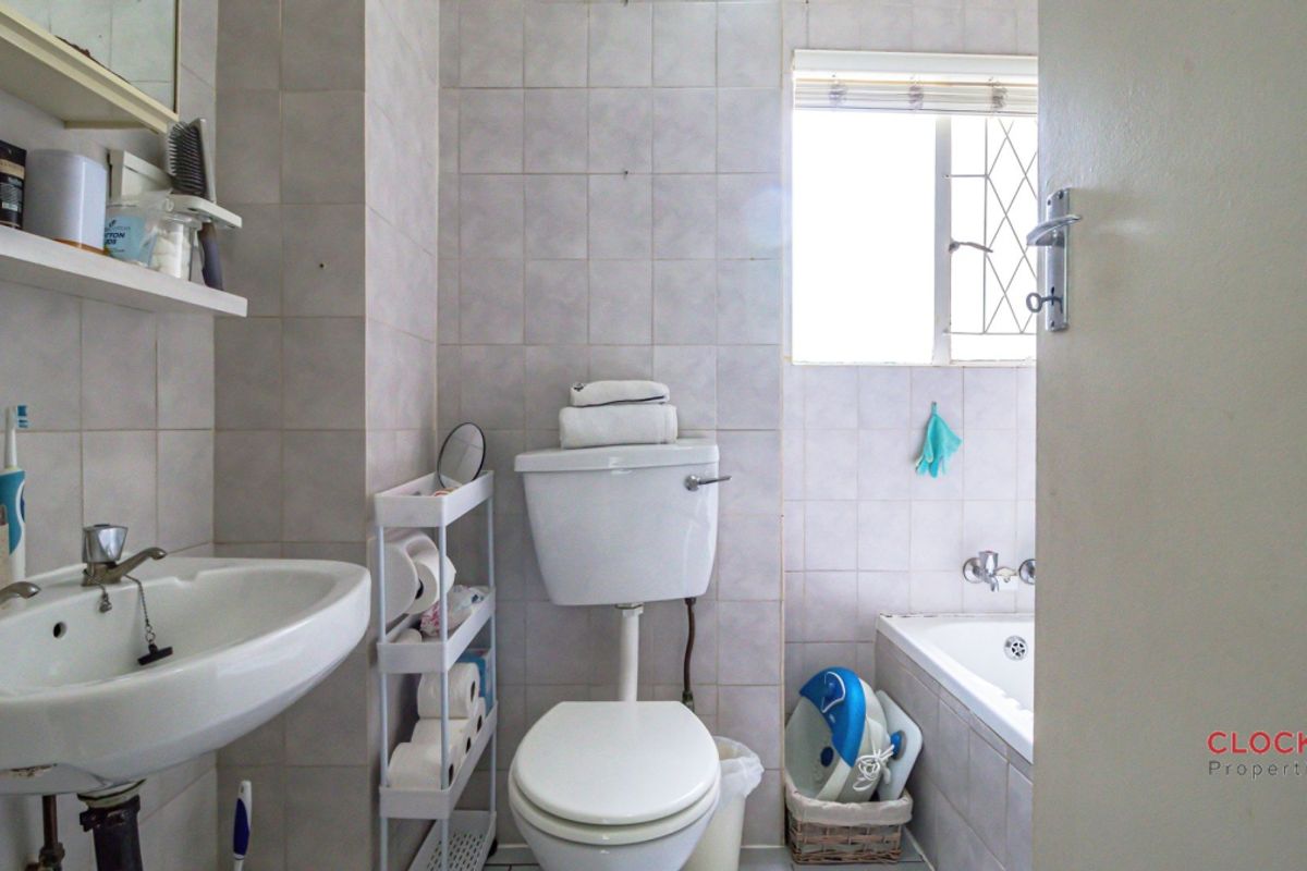 A functional bathroom featuring a standard bathtub, pedestal sink, and toilet, finished with neutral wall tiling and a window for natural light.