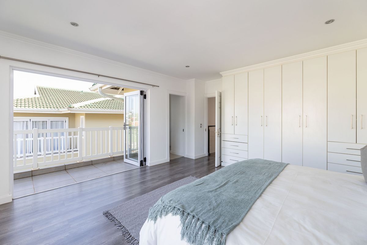 Spacious bedroom featuring extensive built-in cupboards, modern laminate flooring, and bi-fold doors opening onto a private balcony.