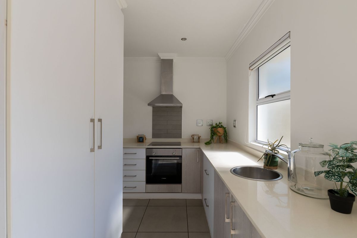 A modern, well-maintained kitchen featuring stone countertops, built-in oven, electric hob, stainless steel extractor fan, and ample cabinetry.