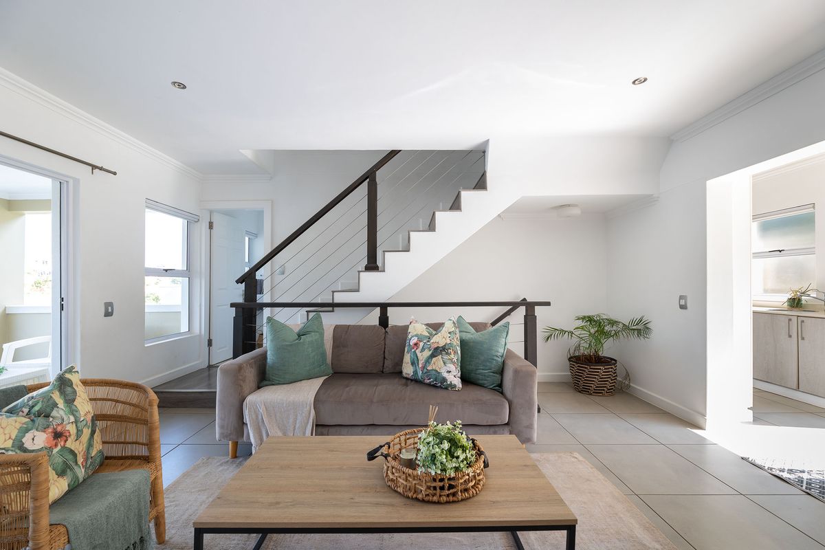 A bright, open-plan living area featuring neutral tiled flooring, a modern staircase with metal balustrades, and direct access to an outdoor patio.