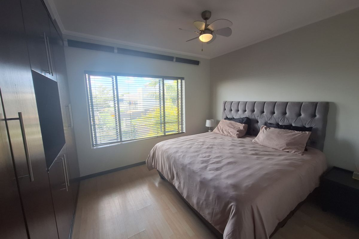 A well-maintained bedroom featuring built-in dark wood cabinetry, light wood-look flooring, and a ceiling fan.