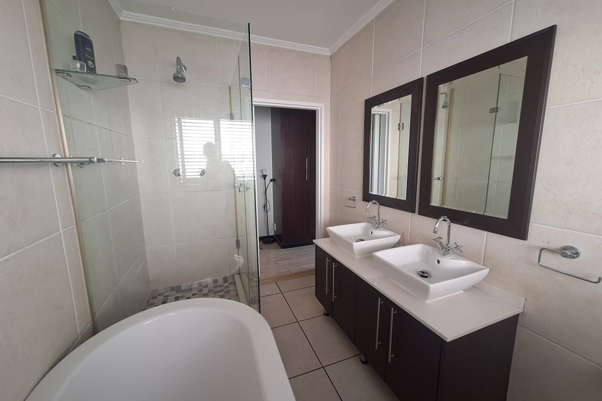 Modern bathroom featuring a double vanity with vessel sinks, a glass-enclosed walk-in shower, and a freestanding bathtub with neutral wall and floor tiling.