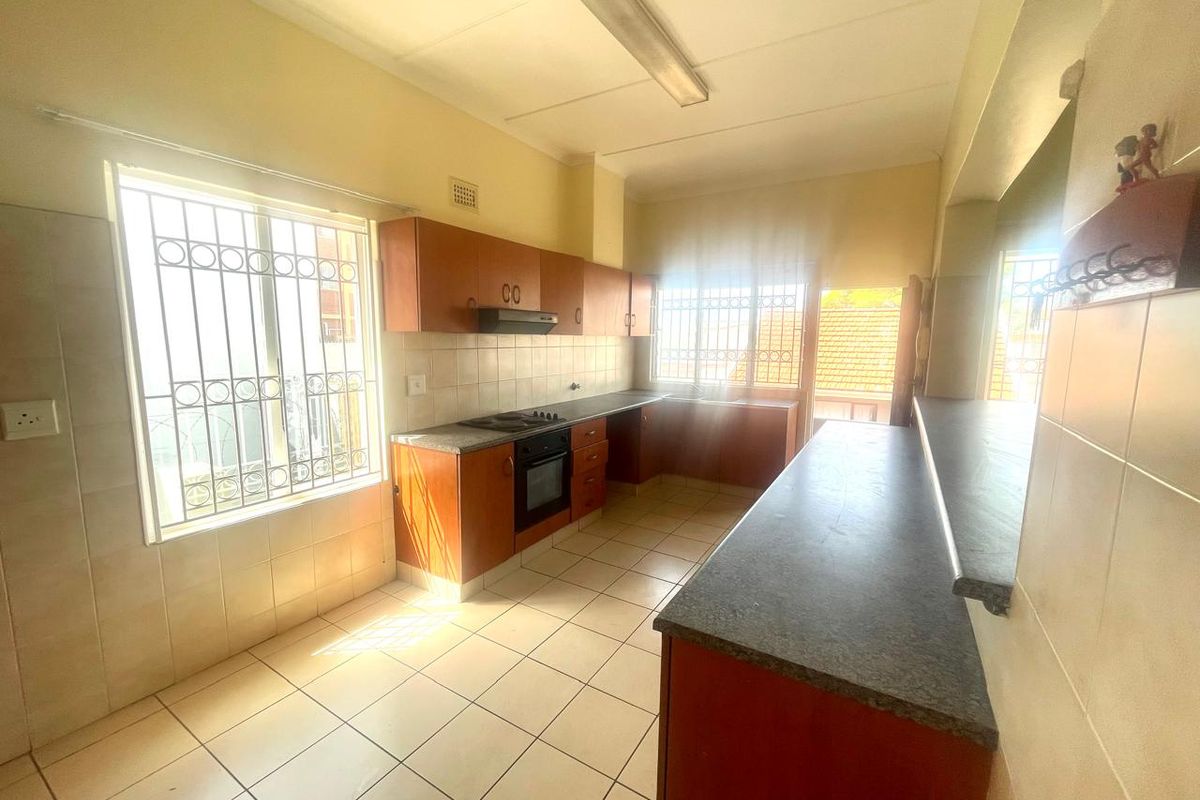 A functional kitchen featuring wooden cabinetry, laminate countertops, built-in oven and hob, tiled flooring, and a breakfast bar with natural light.