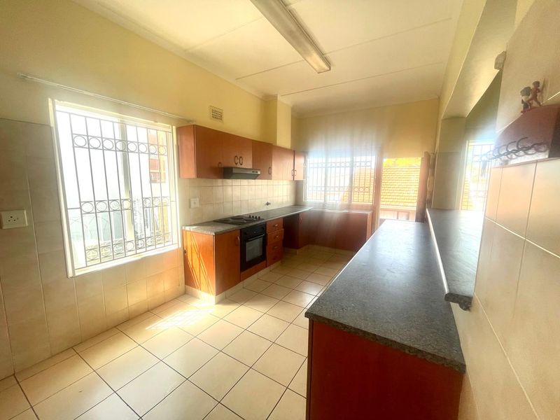A functional kitchen featuring wooden cabinetry, laminate countertops, built-in oven and hob, tiled flooring, and a breakfast bar with natural light.