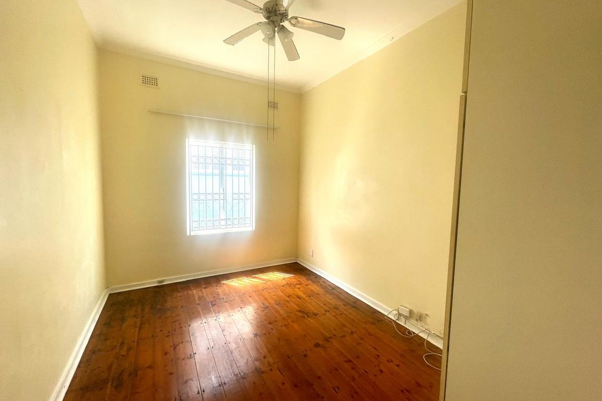An empty bedroom featuring original hardwood flooring, a ceiling fan, and a window fitted with security bars.