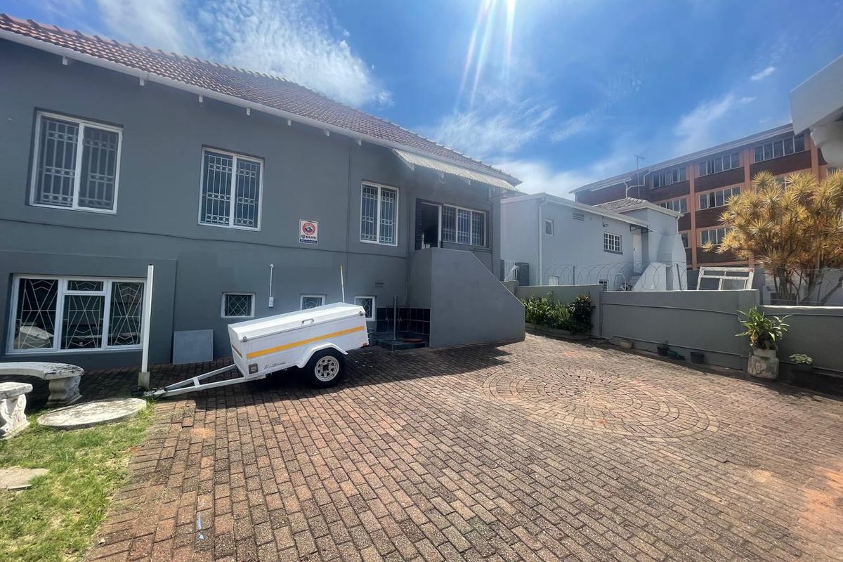 Rear exterior view of the townhouse featuring a paved courtyard, security-fitted windows, and an external staircase leading to the main entrance.