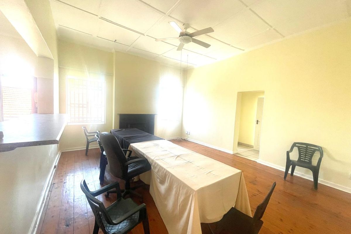 Spacious living area featuring original hardwood flooring, a ceiling fan, and a fireplace, offering a versatile layout for comfortable family living.