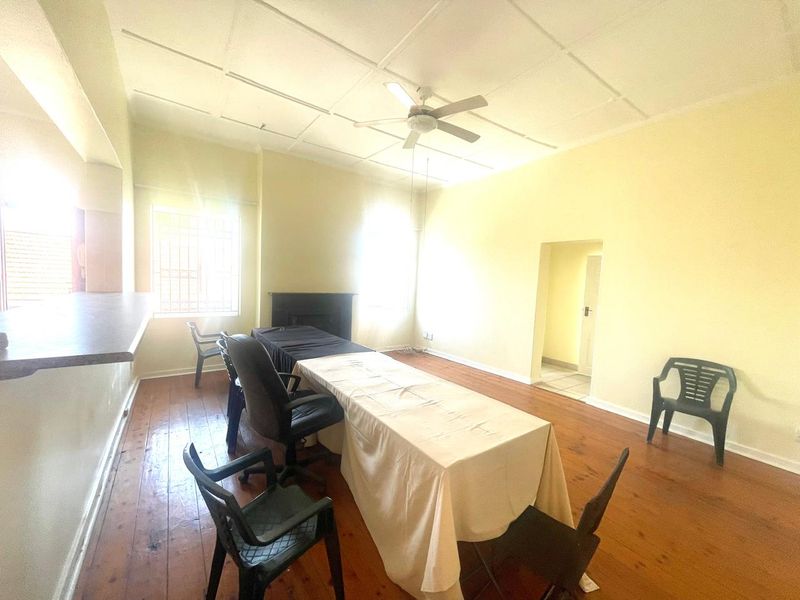 Spacious living area featuring original hardwood flooring, a ceiling fan, and a fireplace, offering a versatile layout for comfortable family living.