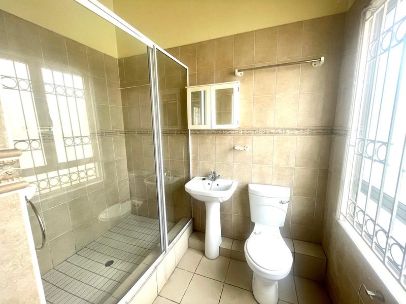 A functional bathroom featuring a pedestal basin, toilet, and a glass-enclosed shower with neutral wall and floor tiling.