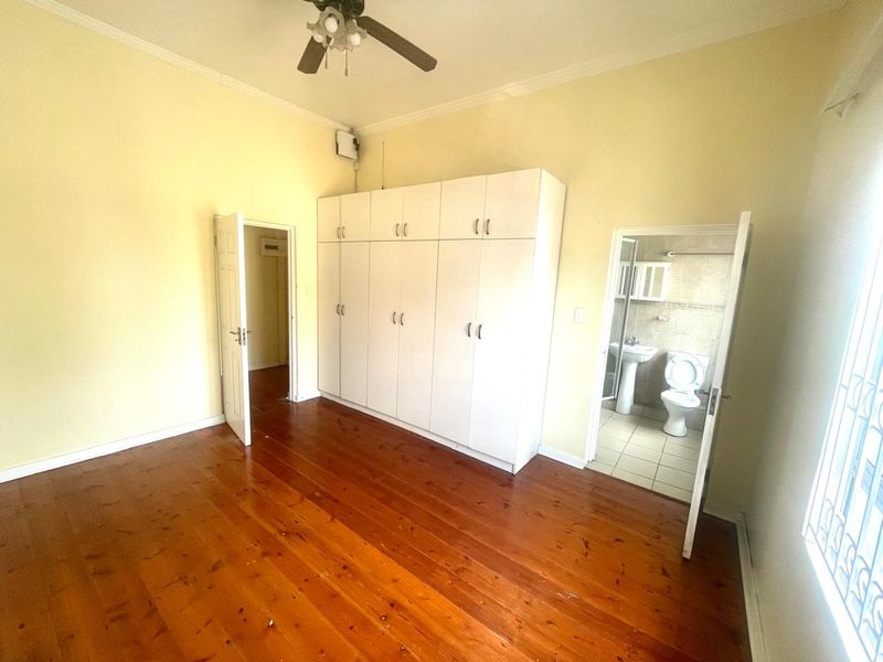 Spacious bedroom featuring polished hardwood floors, extensive built-in cabinetry, and an attached en-suite bathroom.